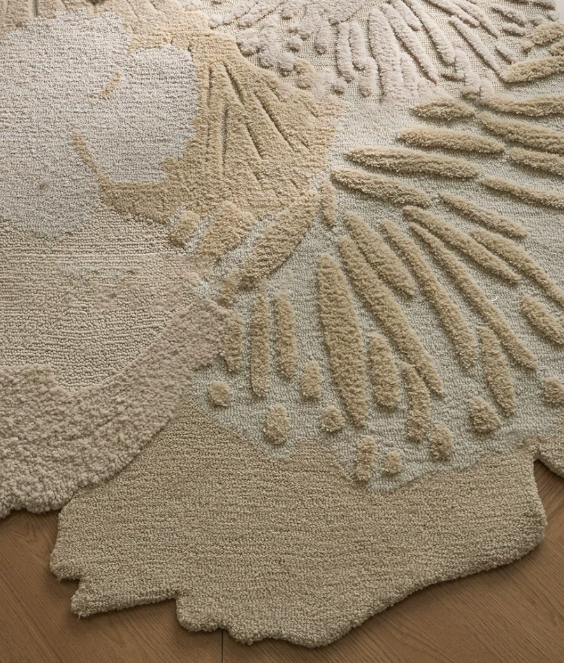 textured area rug with a large abstract floral or sunburst pattern in warm cream and beige tones, laid over a light wood floor.