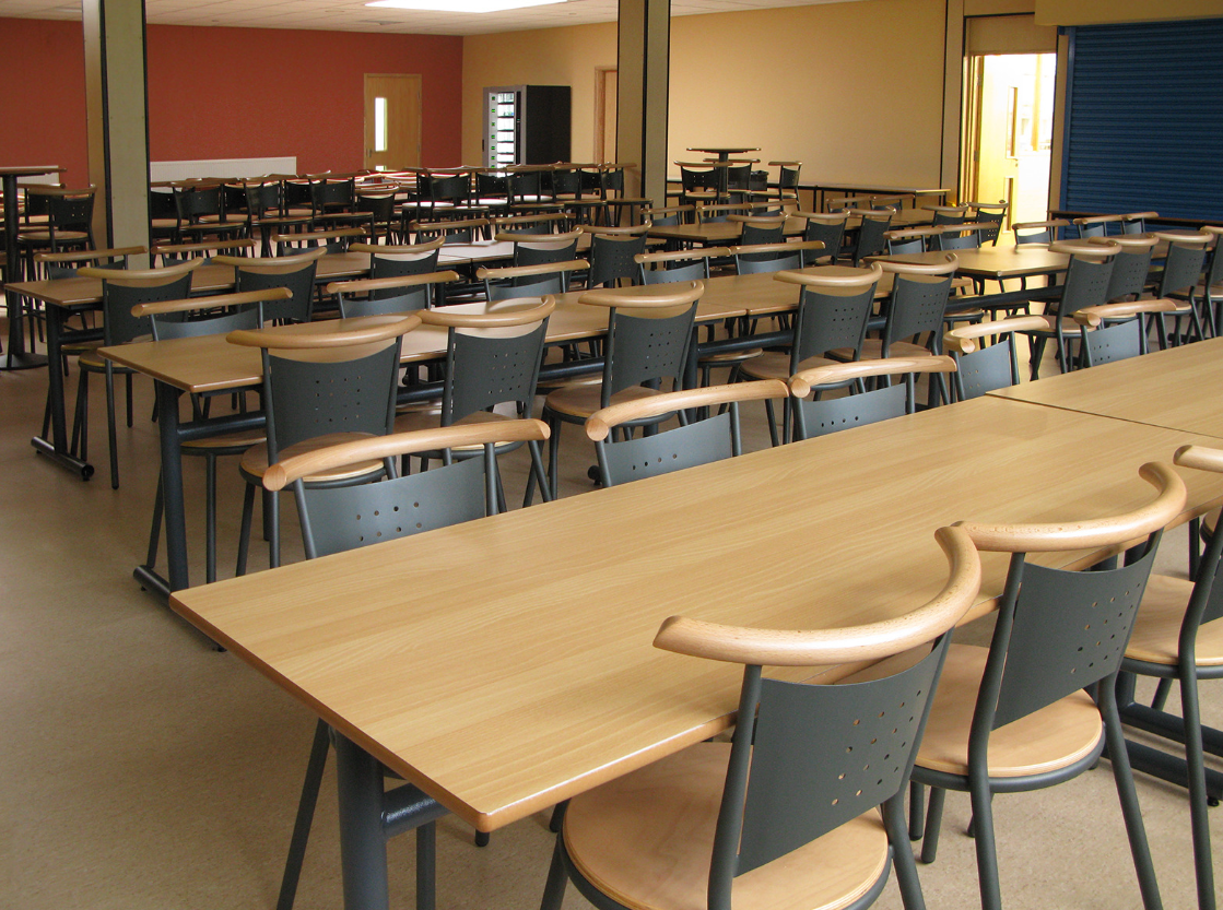 Wooden school tables with gray perforated chairs in a spacious classroom setting, ideal for educational institutions.