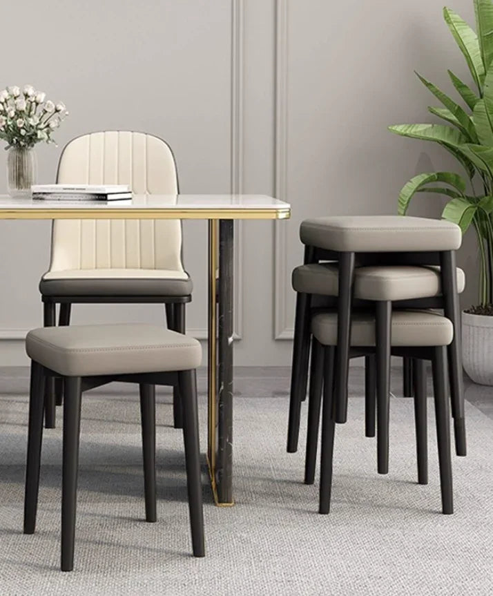 Modern dining chair and stackable stools with cream upholstery, black legs, beside marble table in stylish home setting