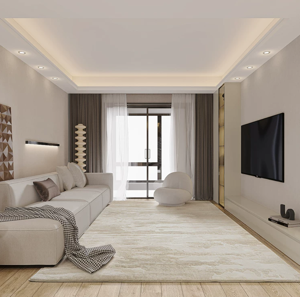 A modern living room rug with a light beige sectional sofa, matching area rug, white accent chair, dark brown curtains, wood flooring, and a wall-mounted flat-screen TV.