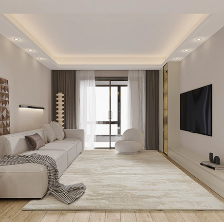 A modern living room rug with a light beige sectional sofa, matching area rug, white accent chair, dark brown curtains, wood flooring, and a wall-mounted flat-screen TV.