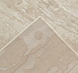Close-up of a textured area rug corner showing a low-pile abstract pattern in warm beige and cream tones.