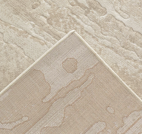 Close-up of a textured area rug corner showing a low-pile abstract pattern in warm beige and cream tones.
